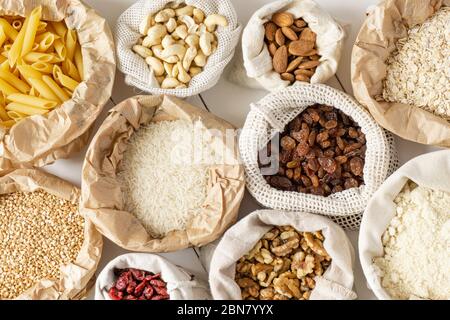 Semole, pasta, noci e frutta secca in sacchetti di carta e cotone su tavola di legno bianco. Vista dall'alto. Zero sprechi, eco-compatibile o concetto di stile di vita senza plastica. Foto Stock