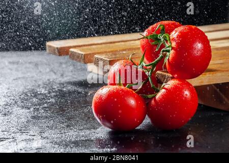 Pomodori maturi sulla tavola di legno su sfondo scuro con spruzzi d'acqua. Foto Stock