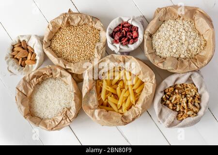 Semole, pasta, noci e frutta secca in sacchetti di carta e cotone su tavola di legno bianco. Vista dall'alto. Zero sprechi, eco-compatibile o concetto di stile di vita senza plastica. Foto Stock