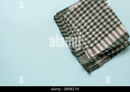 Sfondo turchese chiaro con un asciugamano verde a scacchi. Asciugamano da cucina piegato casualmente. Background minimalistico multitasking. Vista dall'alto. Foto Stock