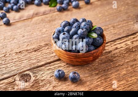 Mirtilli freschi con foglie di mirtillo in ciotola di legno su sfondo di legno. Foto Stock