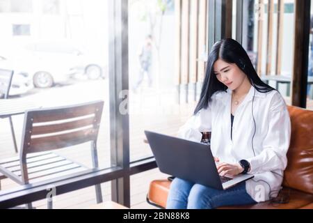 Le donne d'affari asiatiche stanno usando i calcolatori del notebook e indossano le cuffie per le riunioni in linea e lavorare da casa. Foto Stock