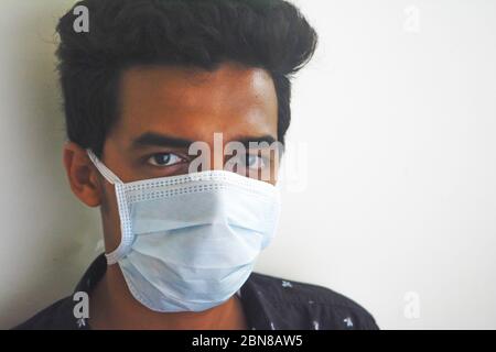Primo piano di un giovane uomo in una maschera facciale per proteggere contro l'infezione da virus corona. Foto Stock