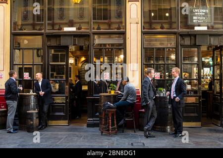 I lavoratori di ufficio di sesso maschile bevono dentro e fuori un pub britannico a Leadenhall Market, Londra, Regno Unito Foto Stock