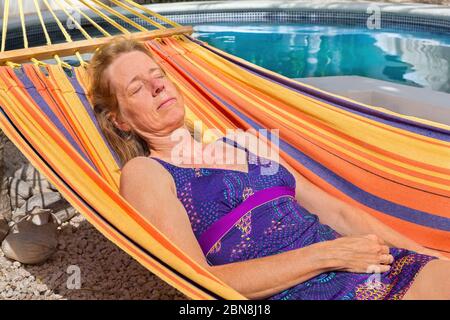 Donna olandese di media età sdraiata in un'amaca colorata vicino alla piscina Foto Stock