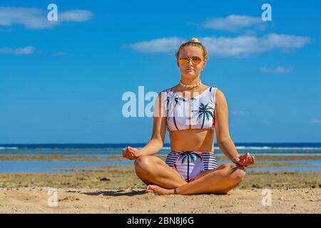 Giovane caucasica in bikini medita sulla spiaggia con mare Foto Stock