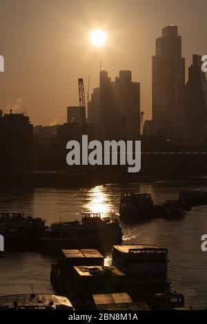 Sunrise a Londra crea una silhouette della City di Londra con il Tamigi e le barche fluviali in primo piano. Foto Stock