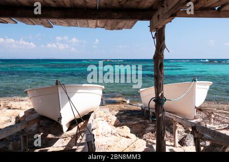 Due piccole barche su rotaie sulla spiaggia rocciosa. Barche sulle caratteristiche rotaie in legno dell'isola di Formentera. Sullo sfondo il Mediterraneo Foto Stock