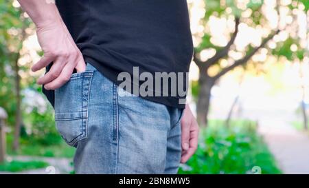 Mano uomo porta il portafoglio nero all'interno della tasca blu jeans denim. Esterno. Foto Stock