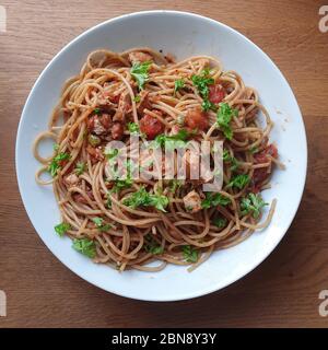 condire il pollo con salsa di pomodoro e prezzemolo in una ciotola bianca su un tavolo di legno Foto Stock