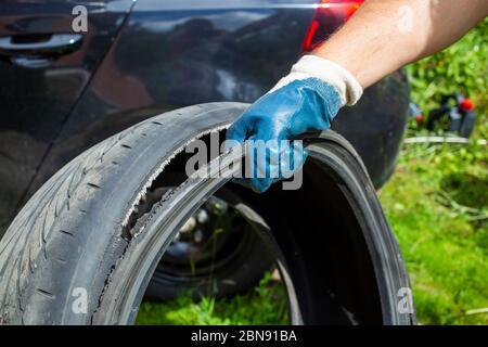 concetto di lavoro muscolare. la mano del maestro in un guanto blu tiene il pneumatico strappato. sullo sfondo auto nera in sfocatura Foto Stock