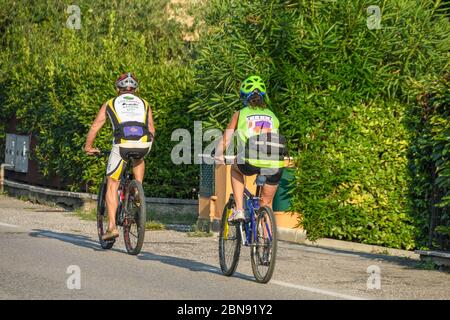 GARDA, ITALIA - SETTEMBRE 2018: Due persone in bicicletta lungo una strada nella città di Garda sul Lago di Garda. Foto Stock