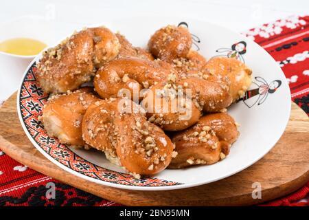 Concetto di cucina rumena. Mucenici fatti in casa, dolci tradizionali fatti nella figura 8 a sembrare ghirlande, cosparsi di miele e noci tritate. Foto Stock