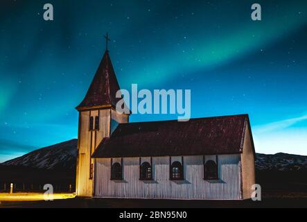 Bella verde e blu aurora boreale danzare su una piccola chiesa del villaggio in Islanda. Foto Stock