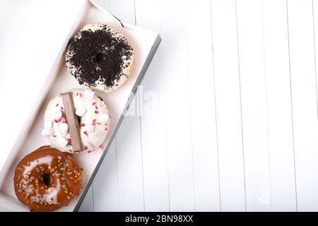 Tre vetri fusi con cioccolato bianco e scuro, marshmallows, crumbles biscotto, ciambelle ricoperte di zucchero caramello su tavola di legno bianco Foto Stock