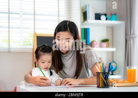 Ragazza studentesca asiatica con pittura madre immagine nel libro con matita a colori a casa, Homeschooling e l'apprendimento a distanza. Foto Stock