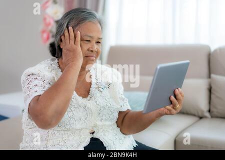 Donna anziana che effettua una videochiamata con il medico con la sua sensazione di mal di testa su tablet digitale online assistenza sanitaria digitale tecnologia consulenza Foto Stock