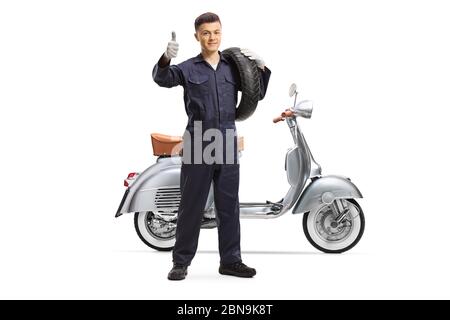 Ritratto a tutta lunghezza di un giovane meccanico che tiene un pneumatico da scooter e mostra pollici isolati su sfondo bianco Foto Stock
