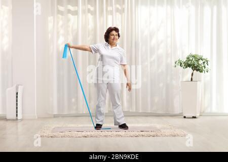 Ritratto a tutta lunghezza di una donna anziana che si esercita con un elastico a casa su un tappetino Foto Stock