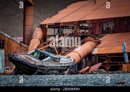 La vecchia barca di legno si trova sulla riva di fronte Edificio in metallo arrugginito sull'Isola di Stomness Foto Stock