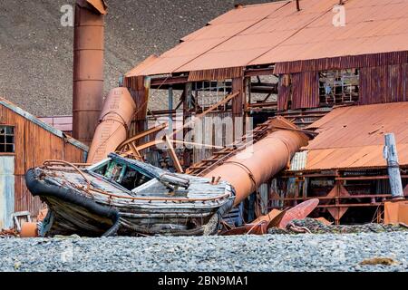 La vecchia barca di legno si trova sulla riva di fronte Edificio in metallo arrugginito sull'Isola di Stomness Foto Stock