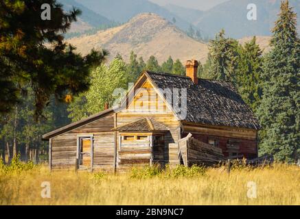 Una cabina di legno abbandonata si trova tranquillamente in un prato d'autunno con montagne sullo sfondo. Foto Stock