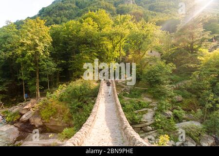 Uomo che attraversa il ponte medievale della verzasca 'Ponte dei salti' Foto Stock