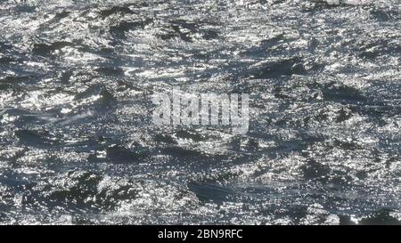 Molti riflessi luminosi del sole sulla superficie dell'acqua di mare. Primo piano dell'oceano con piccole increspature in una giornata di sole. Foto Stock