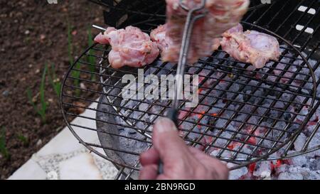 Mano dell'uomo che usa le pinze per girare la carne di pollo sulla griglia per barbecue. Cucina all'aperto. Foto Stock