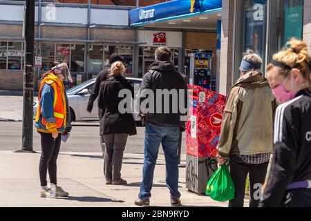 Montreal, CA - 13 maggio 2020: Clienti in una linea al di fuori di una farmacia durante la pandemia di Covid-19. Alcune di esse indossano maschere di protezione Covid-19. Foto Stock