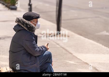 Montreal, CA - 13 maggio 2020: Uomo con maschera facciale per la protezione dal COVID-19 seduto su una panca Foto Stock