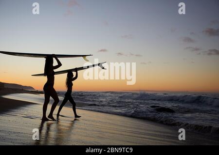 Ragazze che si addentravano per il Sunset Surf sulla North Shore Alle Hawaii Foto Stock