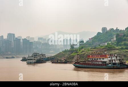 Fengdu, Chongqing, Cina - 8 maggio 2010: Fiume Yangtze. Gruppo di barche ormeggiate più vecchie e arrugginite e 1 rifornimento presso il distributore di benzina galleggiante vicino al litorale verde Foto Stock