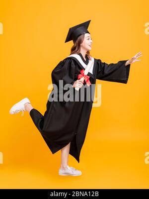 felice giovane donna in abiti di laurea e corsa Foto Stock