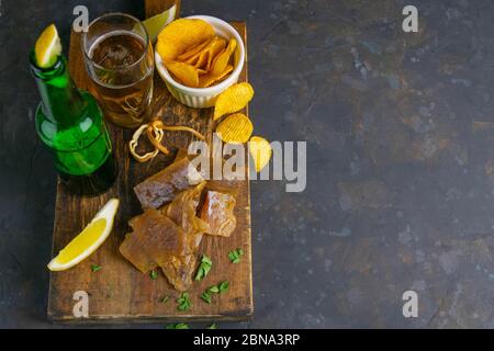 Filetto di pesce gatto essiccato con birra, limone e patatine su tavola di legno scuro. Snack sul pesce con birra. Viste dall'alto con spazio libero Foto Stock