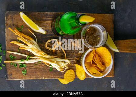 Formaggio con birra, limone e patatine su tavola di legno scuro. Snack sul pesce con birra. Viste dall'alto, primo piano Foto Stock