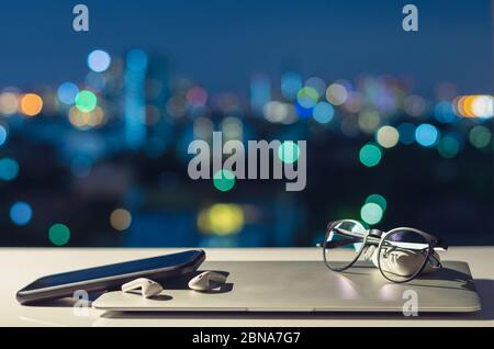 Laptop, smartphone e auricolari si spengono messi sul tavolo con colorate luci da bokeh per disintossicazione digitale, disconnetti sociali, dipendenza da gadget, ecc. Foto Stock