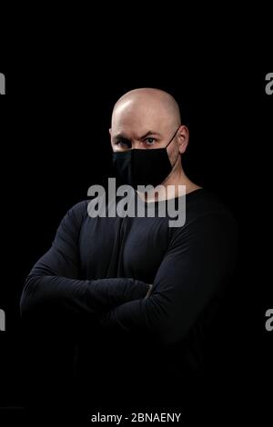 Un uomo in una maschera protettiva nera contro una malattia infettiva, un coronavirus. Foto di studio su sfondo nero Foto Stock