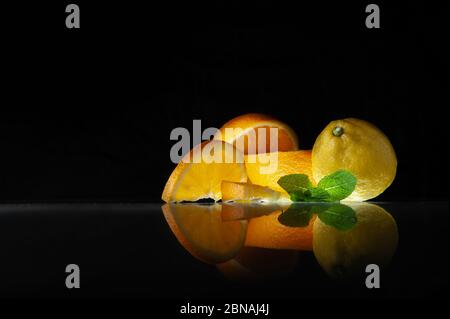 Foglie di menta e arancio di limone affettato con spicchi giacciono su uno sfondo nero Foto Stock