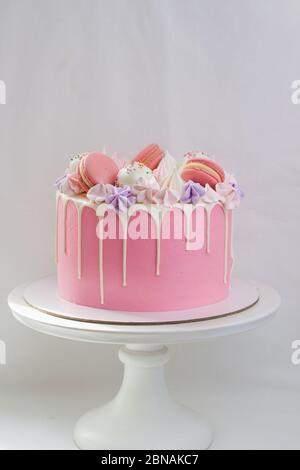 Dolce rosa decorato con cioccolato bianco fuso, macaroon, meringhe, torte pop e caramelle su cakestand bianco. Sfondo semplice. Foto Stock