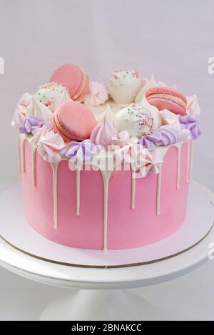 Dolce rosa decorato con cioccolato bianco fuso, macaroon, meringhe, torte pop e caramelle su cakestand bianco. Sfondo semplice. Foto Stock