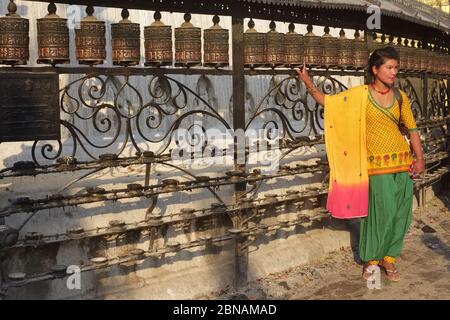 Durante le sue circumdeambulazioni del Tempio di Swayambhunath, Kathmandu, Valle di Kathmandu, Nepal, una visitatrice femminile si pone di fronte a una fila di ruote di preghiera Foto Stock