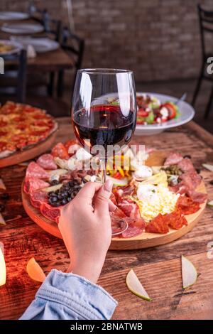 Colpo verticale di una persona che tiene un bicchiere di vino dietro un assortimento di carne Foto Stock