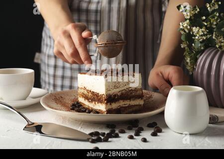 La ragazza spruzzi la polvere su tiramisù. Composizione con gustosa torta su sfondo bianco Foto Stock