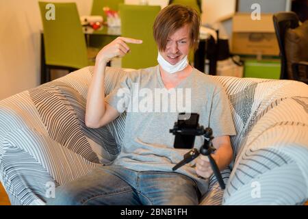 Stressato giovane uomo vlogging e puntando ai capelli mentre in quarantena a casa Foto Stock