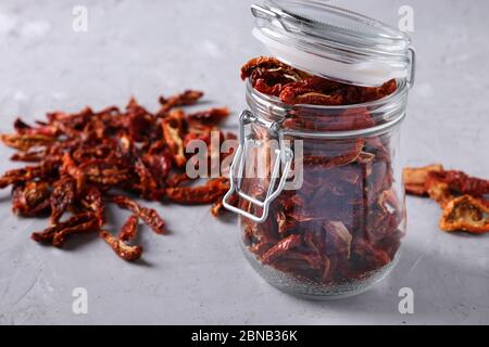 Pomodori secchi con un vaso di vetro su fondo grigio di cemento. Formato orizzontale Foto Stock