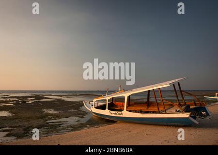 Vista orizzontale del tramonto di una barca pendente aground sulla spiaggia a causa della bassa marea, Gili Air, Isole Gili, Indonesia Foto Stock