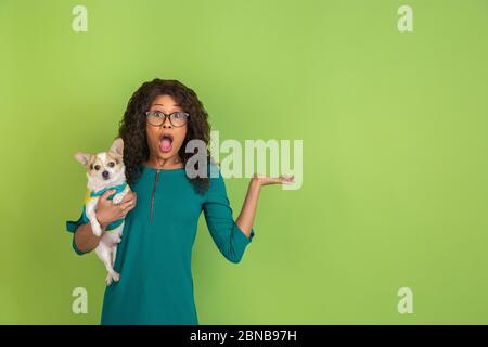 Scioccato, stupito. Ritratto di giovane donna afroamericana isolato su sfondo verde dello studio. Bella femmina riccia modello. Concetto di emozioni umane, espressione facciale, vendite, pubblicità. Foto Stock