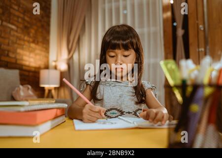 ragazza che studia nella sera. bambino asiatico piccolo che impara a casa che scrive su un libro Foto Stock