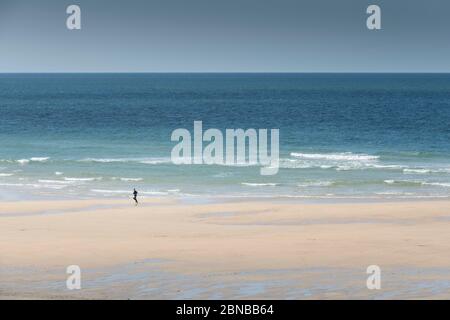 Una persona sola che corre lungo la riva di Fistral Beach a Newquay in Cornovaglia. Foto Stock